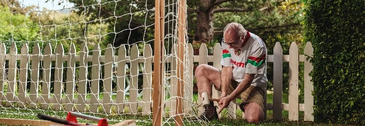 Eine Person baut mit einem Hammer ein Fußballtor im Garten auf.